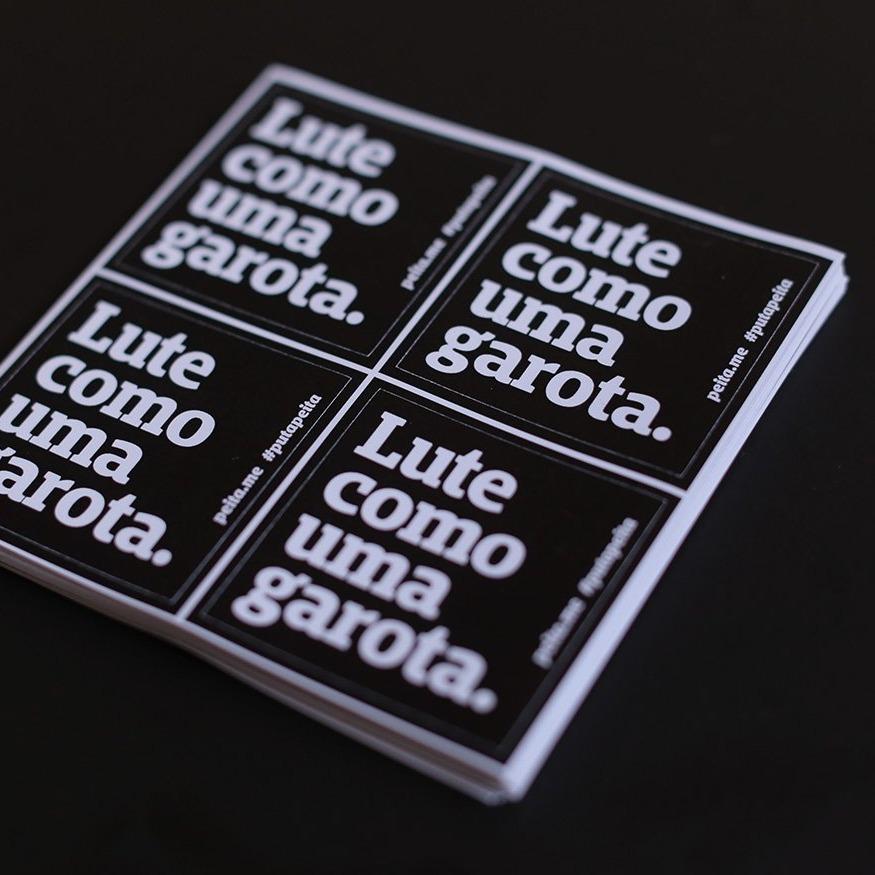 Foto preta e branca de uma cartela com quatro adesivos pretos escrito lute como uma garota em branco.