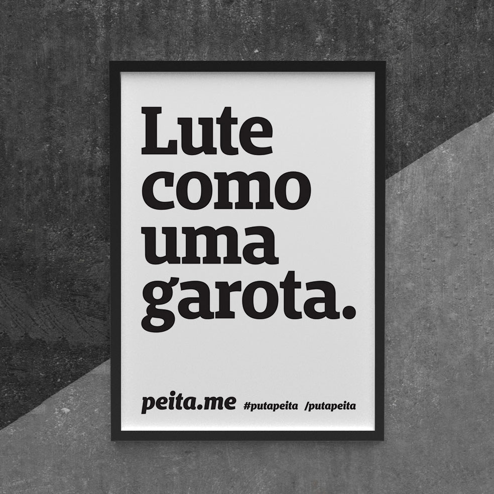 Quadro com moldura preta e frase Lute como uma garota também em preto e fundo branco, frase peita.me #putapeita / putapeita em preto na parte inferior do cartaz. Fundo parede preta com parte cinza.