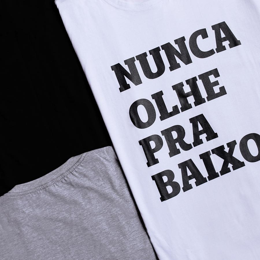 Foto colorida de camiseta branca escrito nunca olhe para baixo em preto.Se vê um pedaço de camisetas preta e cinza.