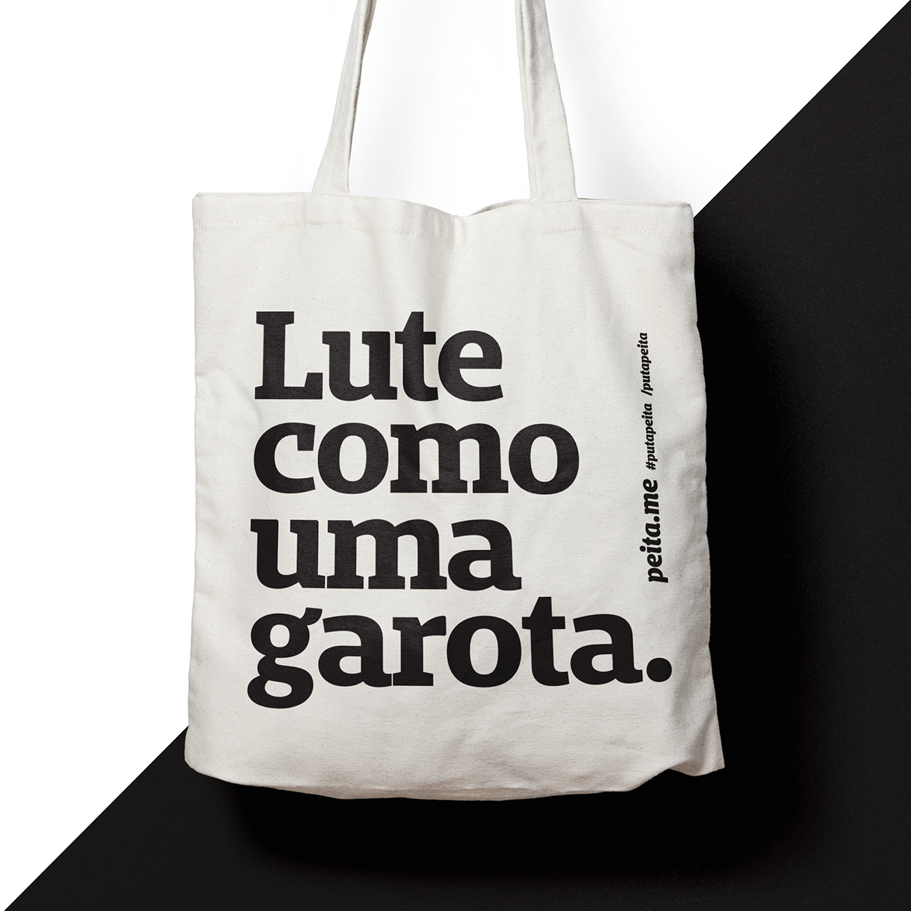 Foto colorida  de uma ecobag de algodão cru  escrito lute como uma garota em preto. O fundo é preto e branco.  