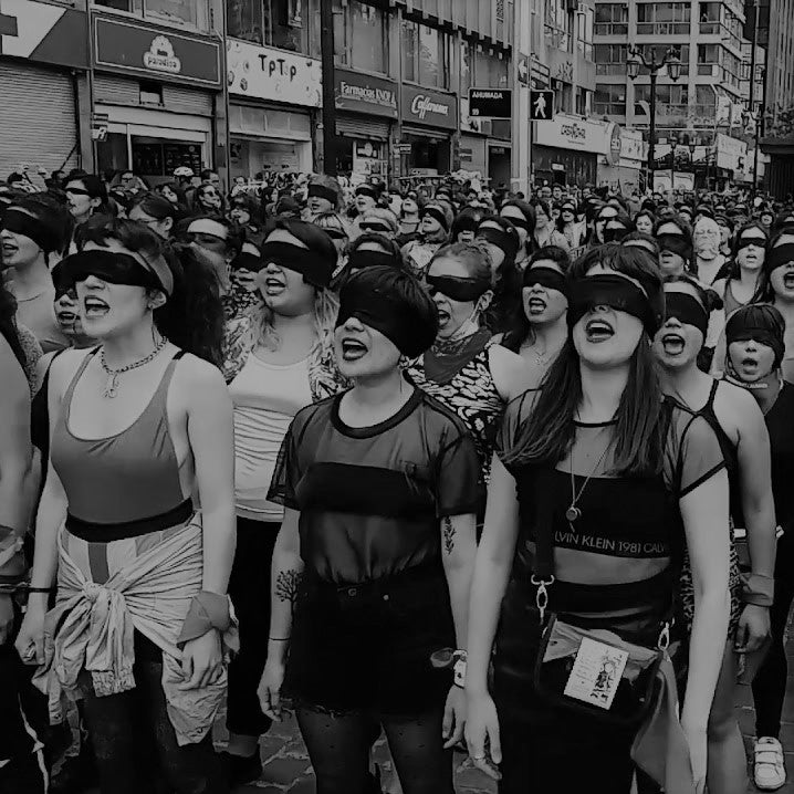 foto preto e branco de dezenas de mulheres com vendas pretas falando. 