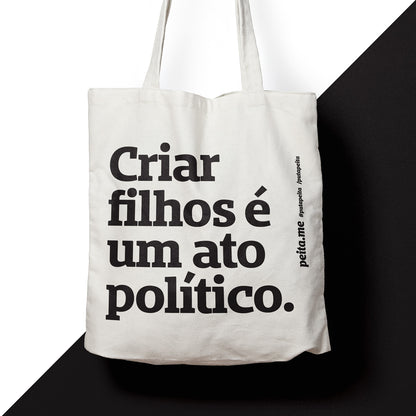Foto colorida de uma ecobag de algodão cru escrito criar filhos é um ato político em preto. O fundo é preto e branco.