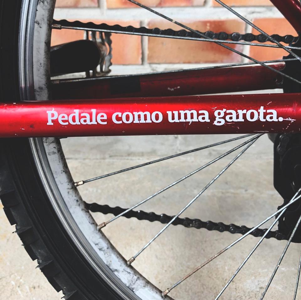 Foto colorida de bicicleta vermelha com adesivo escrito pedale como uma garota em branco. Close na roda traseira. 