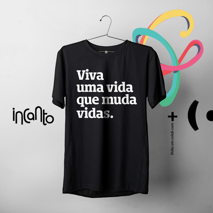 Foto colorida de uma camiseta preta escrito viva uma vida que muda vidas em branco, pendurada em um cabide preto.  fundo cinza claro com logo da Peita em preto.
